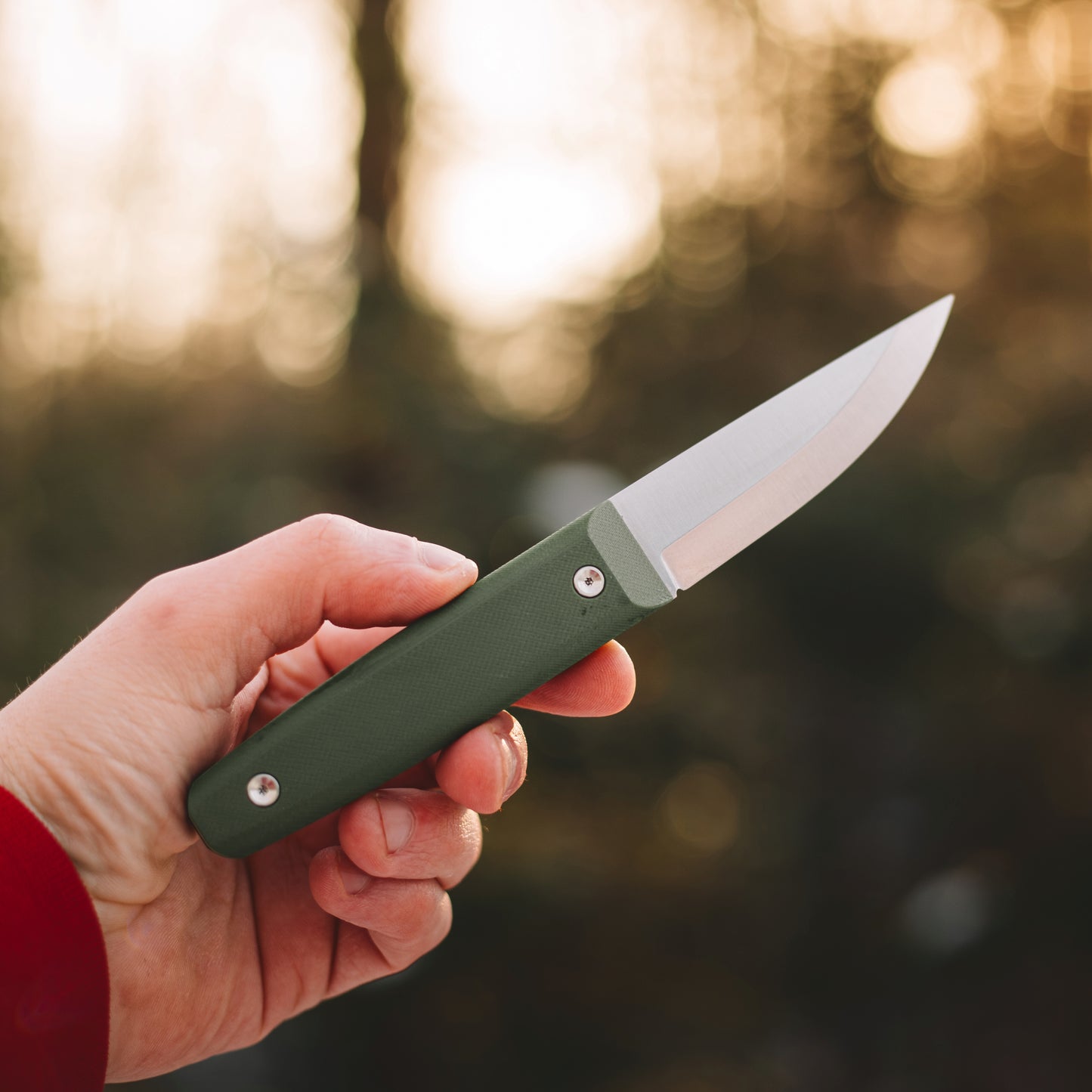 Hand holding a green folding knife with a blurred natural background