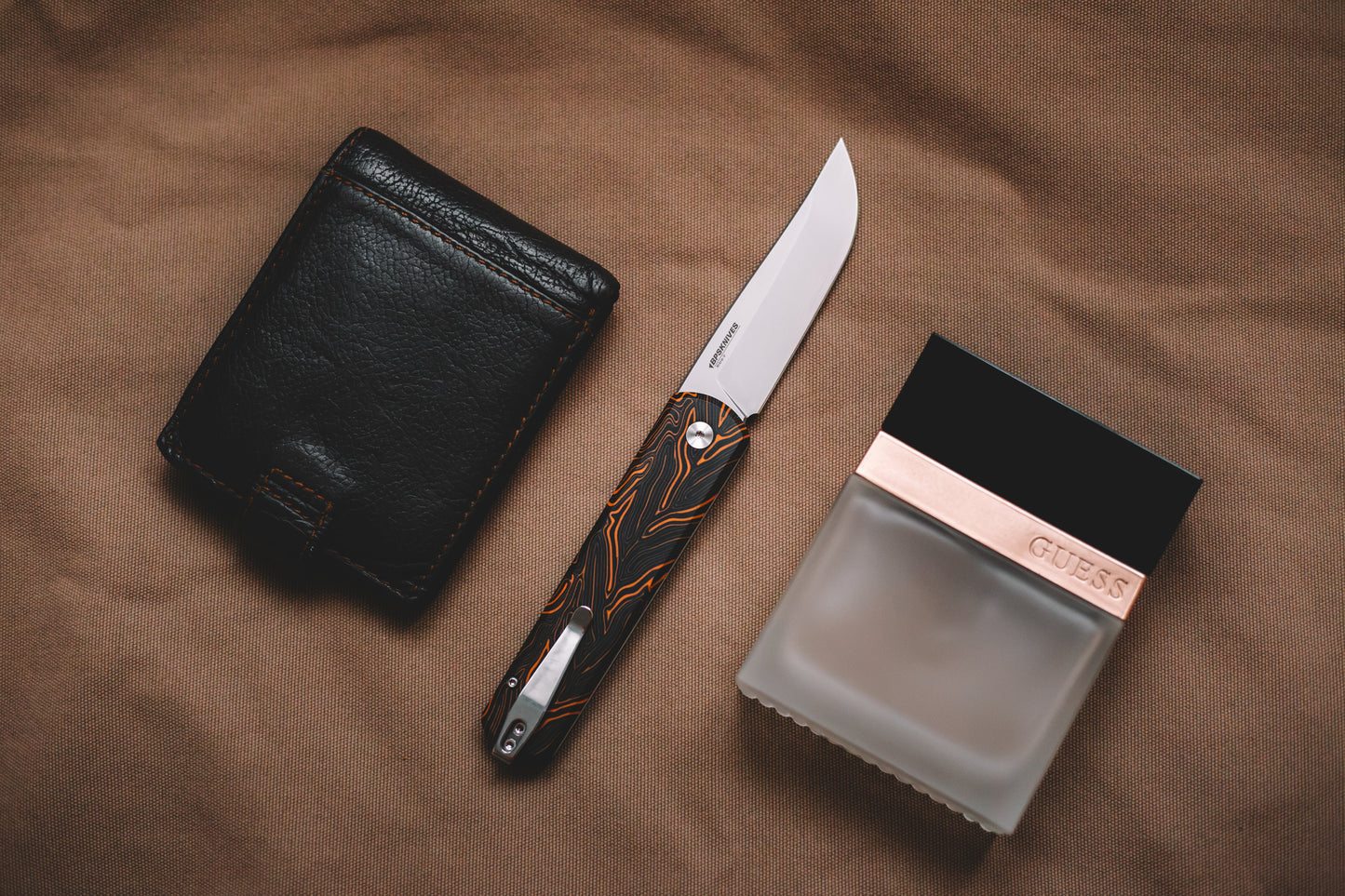 Black leather wallet, knife, and black box on a brown fabric background