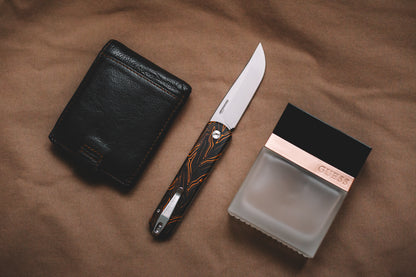 Black leather wallet, knife, and black box on a brown fabric background
