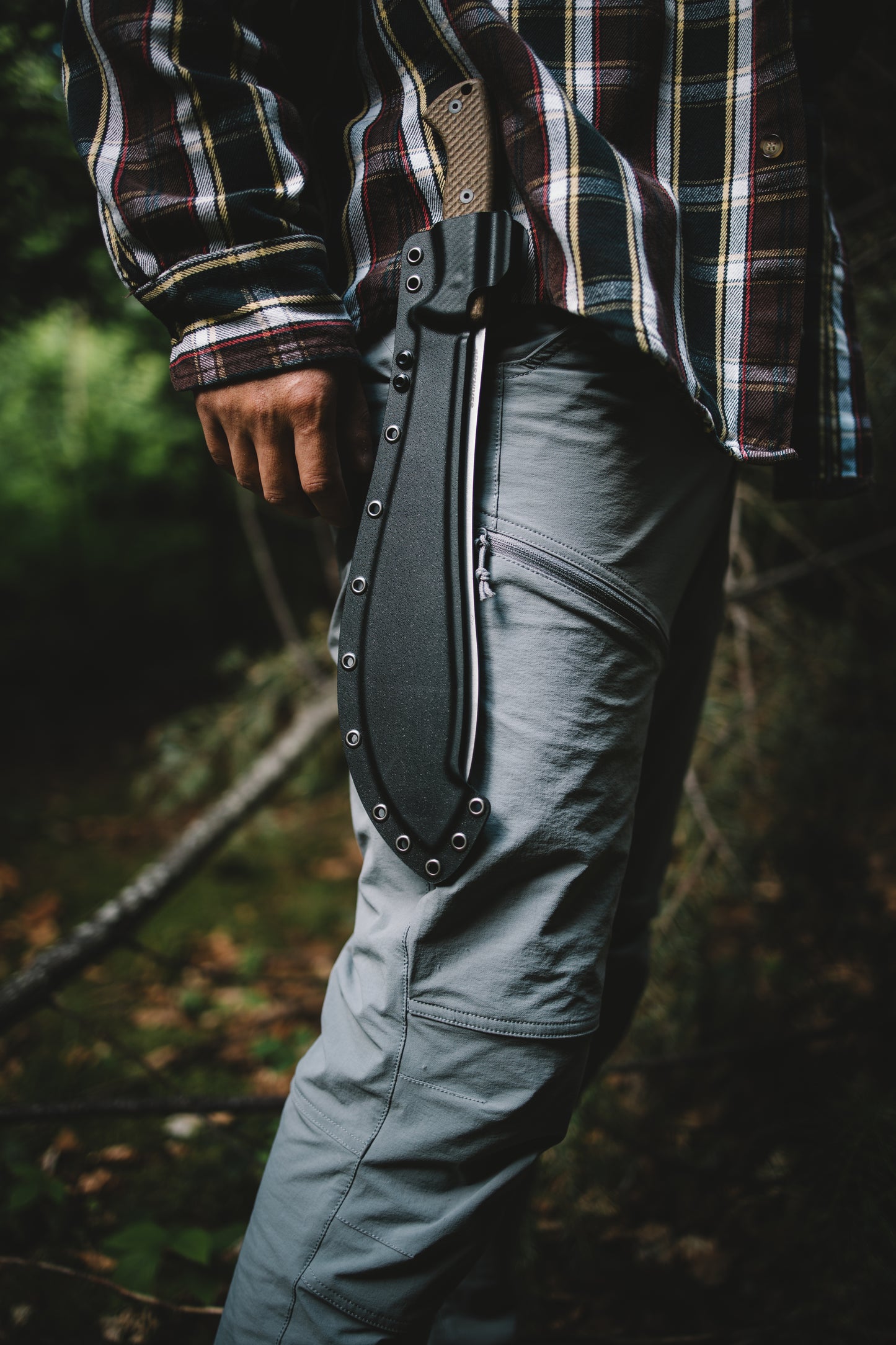 Person wearing a plaid shirt and dark pants with a belt in a forest setting