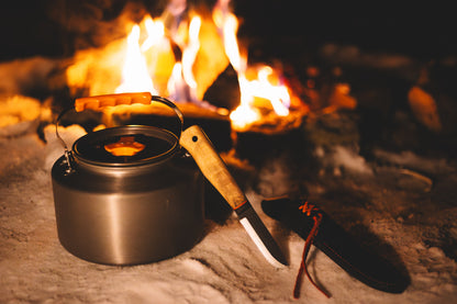 Black camping kettle and knife by a campfire
