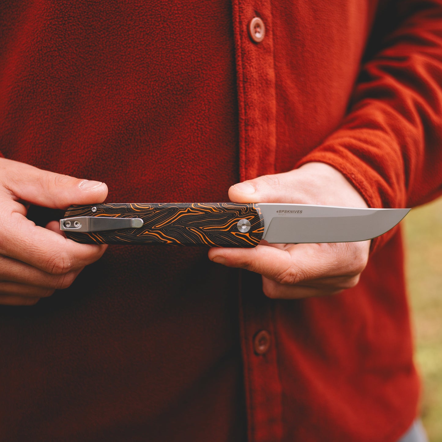 Person holding a folding knife with a detailed handle in an outdoor setting