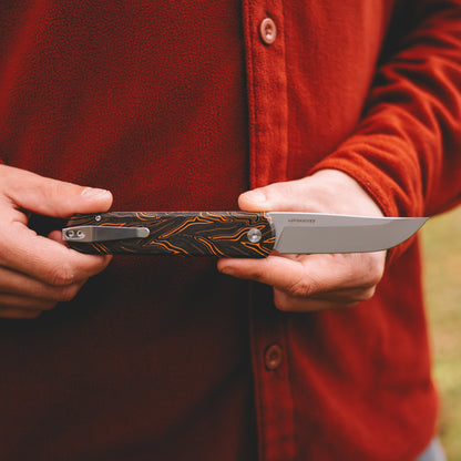 Person holding a folding knife with a detailed handle in an outdoor setting