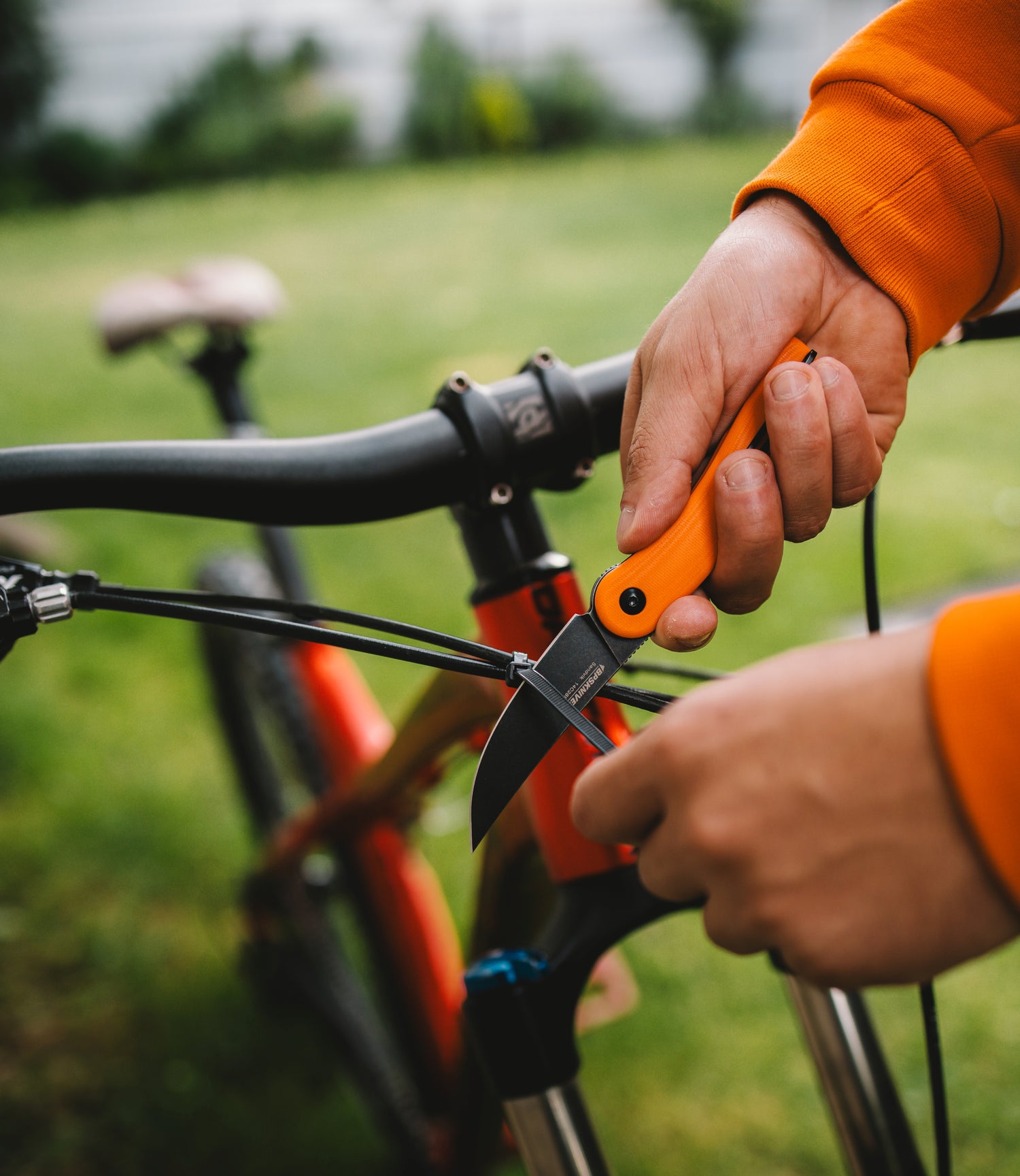 Person holding an orange pocket knife near a bicycle outdoors
