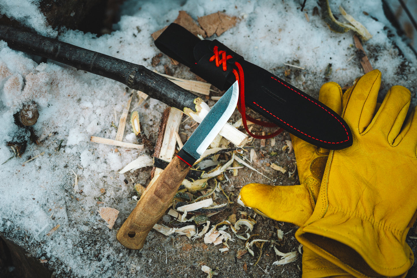 Knife with black sheath and yellow glove on a snowy ground