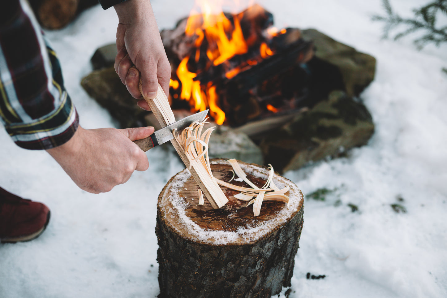 Person splitting wood with a knife over a campfire in the snow