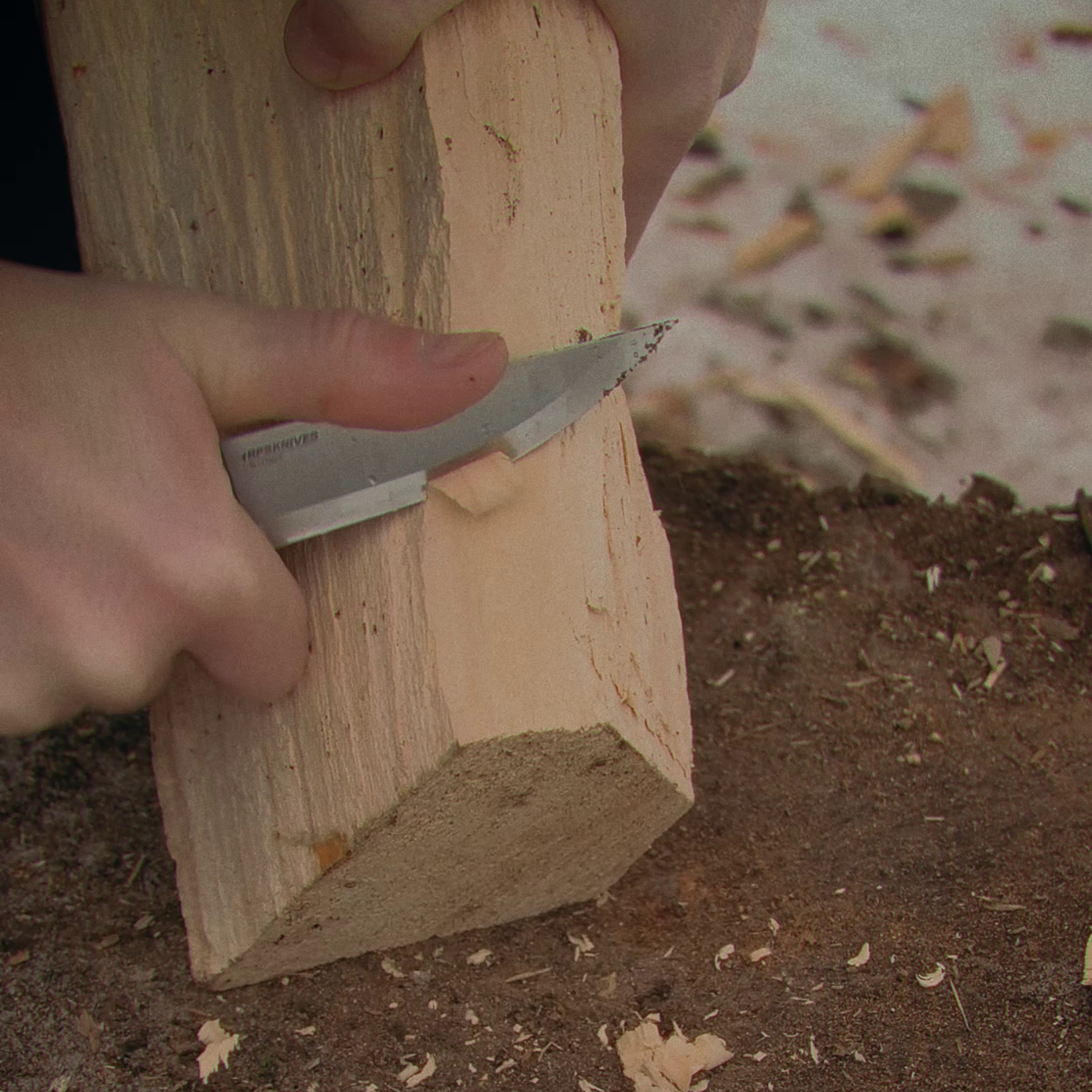 Person using a chisel on a wooden block outdoors