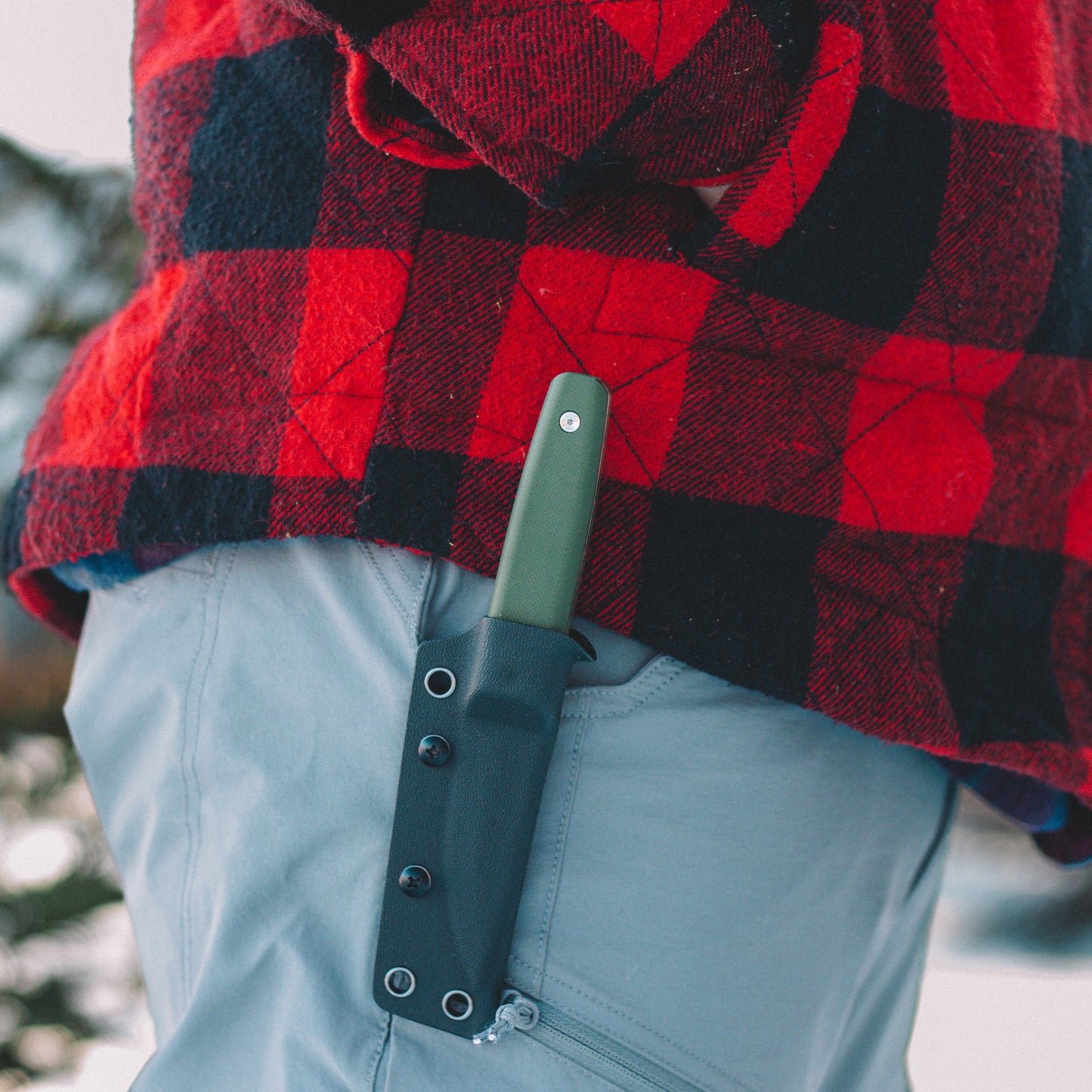 Person wearing a red and black checkered jacket with a green knife sheath on light blue pants.