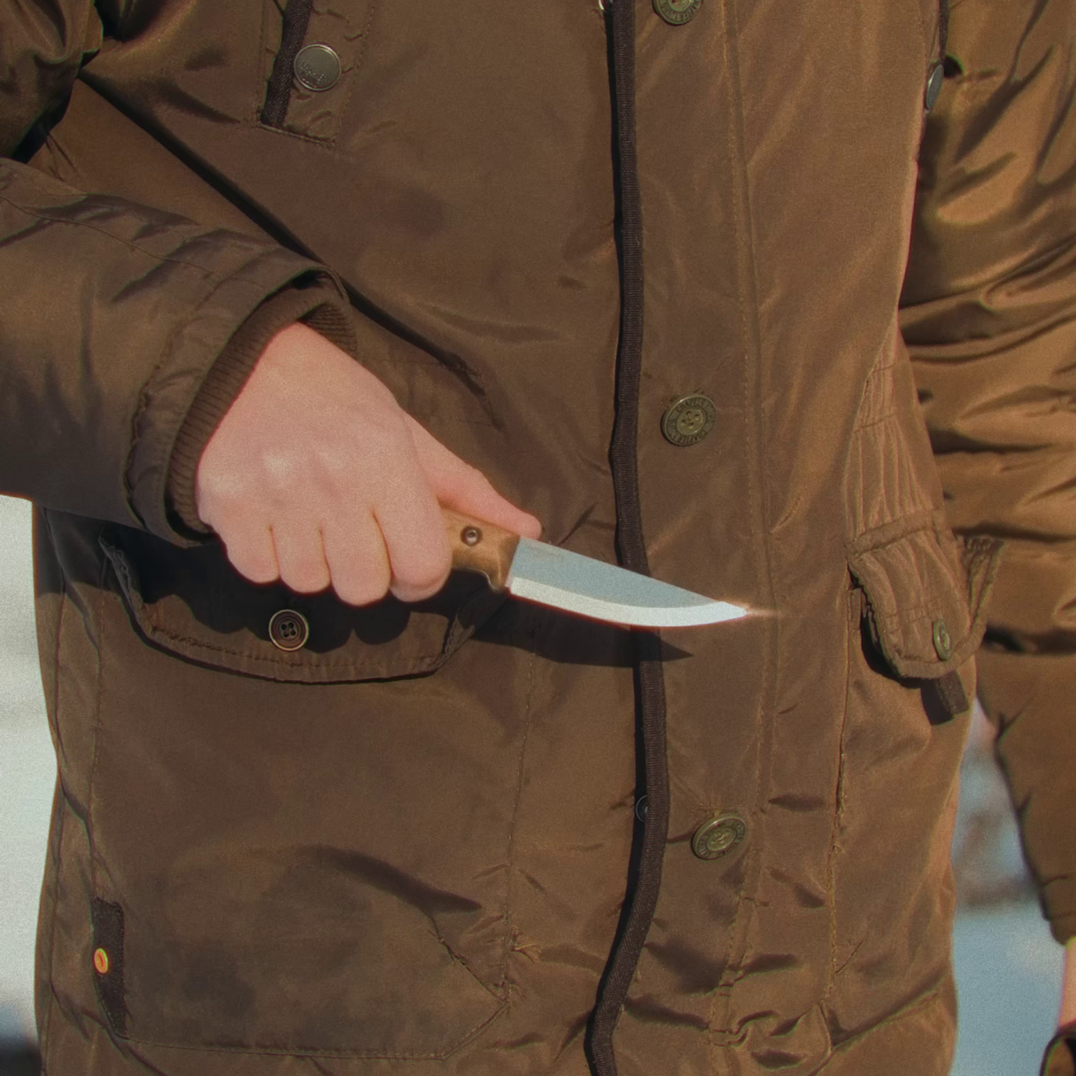 Person in a brown coat holding a knife with a blurred background
