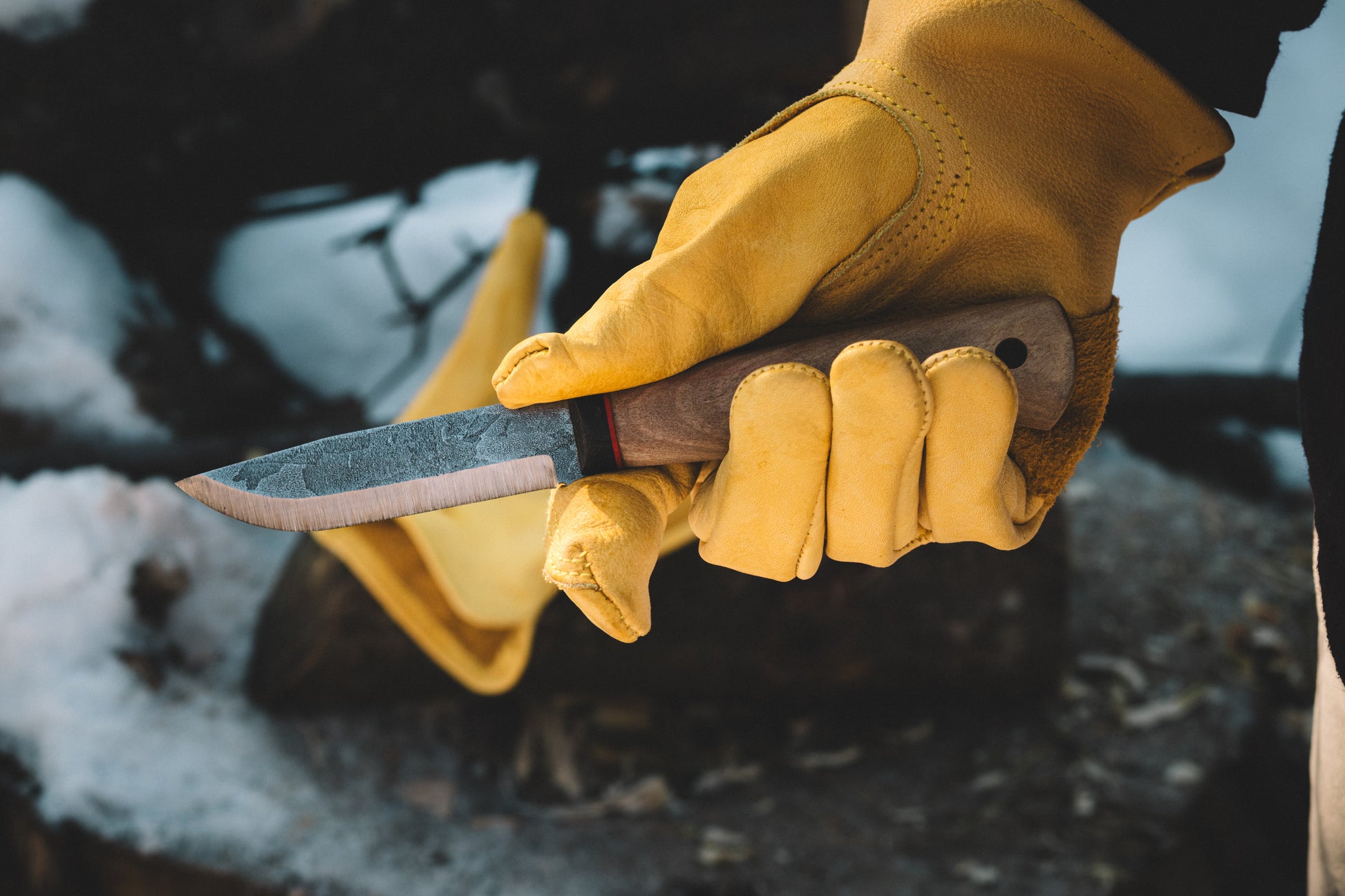 Hand wearing a yellow glove holding a knife with a blurred background