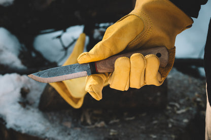 Hand wearing a yellow glove holding a knife with a blurred background