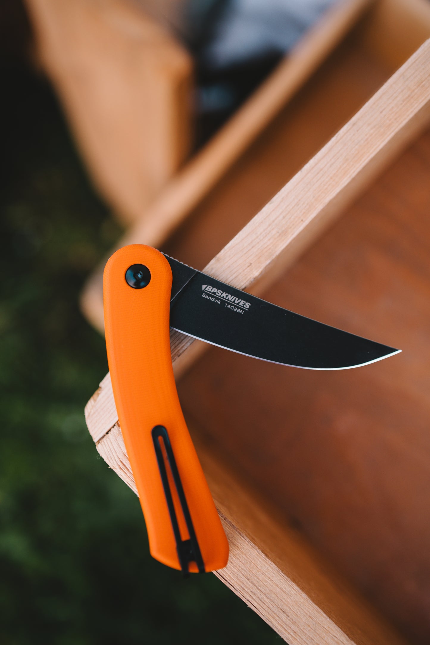 Orange folding knife with black blade on a wooden surface