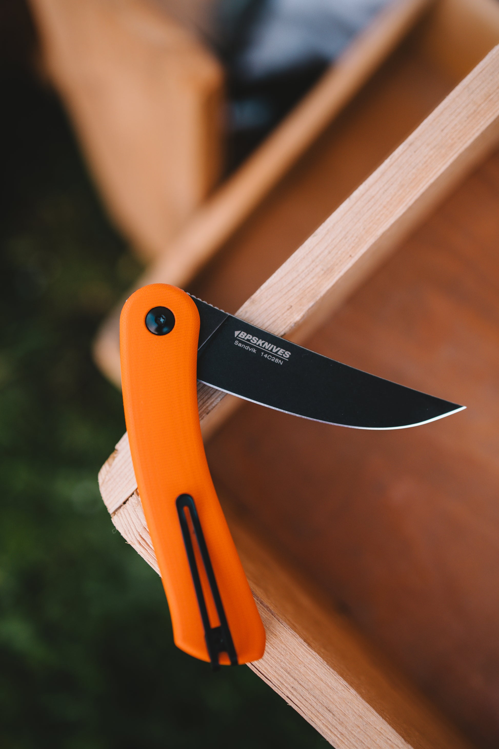 Orange folding knife with black blade on a wooden surface