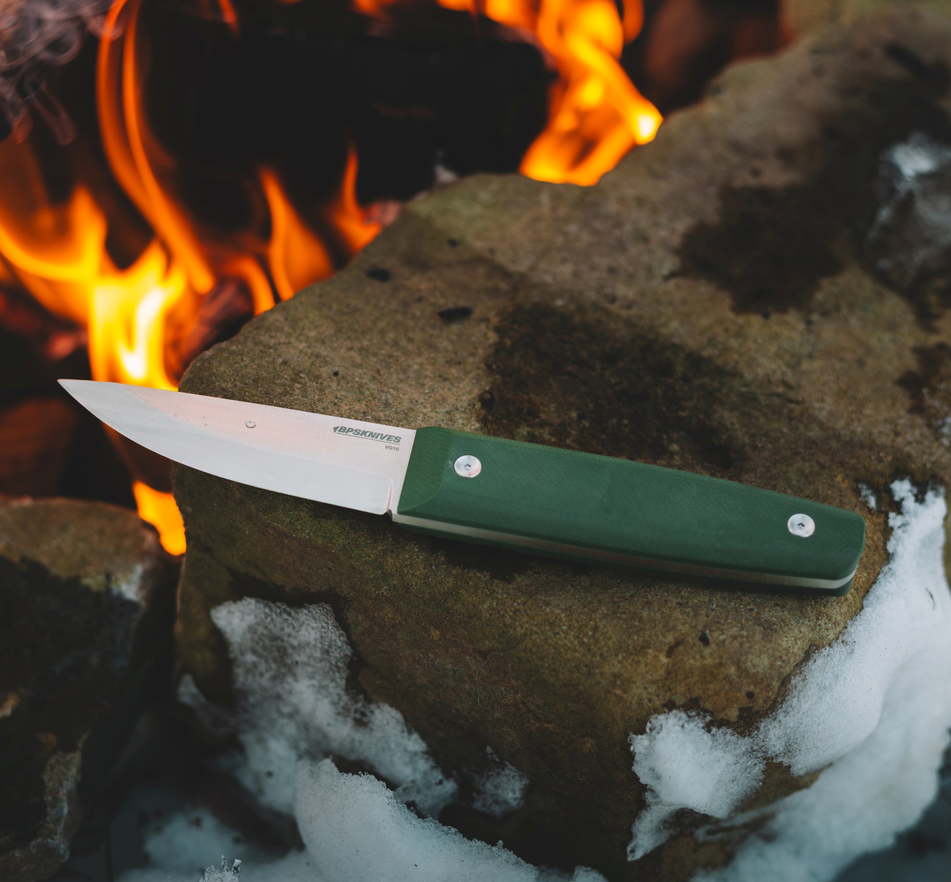 Knife with a green handle on a rock near flames