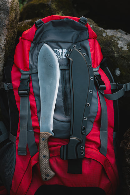 Red backpack with a machete attached, set against a natural rock background