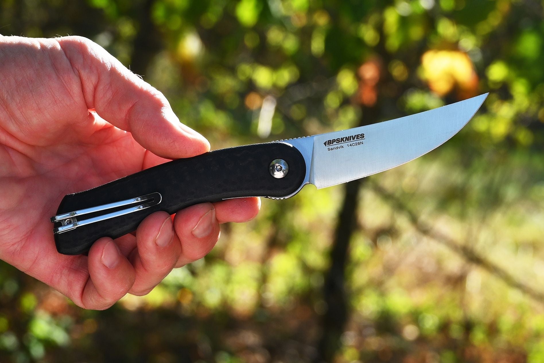 Hand holding a folding knife with a blurred natural background