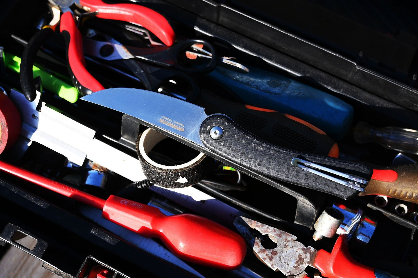 Close-up of a toolbox with various tools including a knife, screwdriver, and pliers.