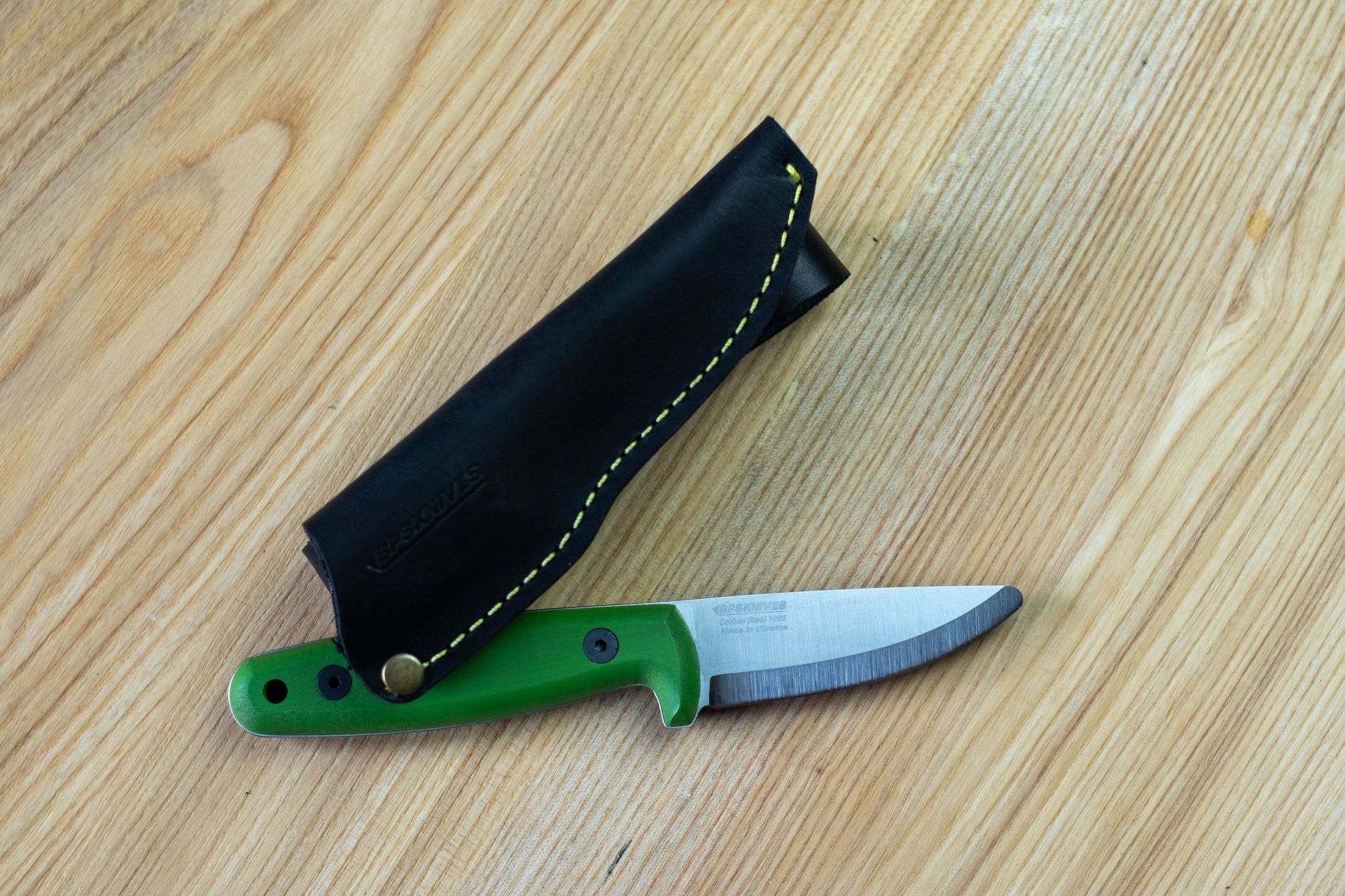 Knife with green handle and black sheath on a wooden surface