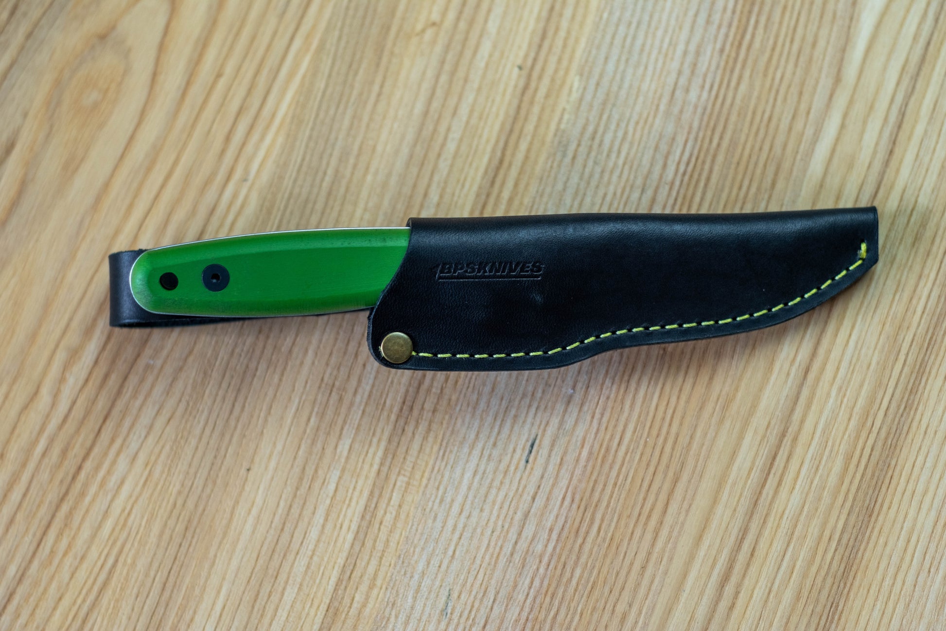 Knife with green blade and black sheath on a wooden surface