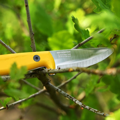 Yellow pocket knife with a silver blade on a branch against a green leafy background
